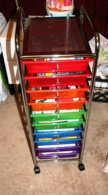 A rolling storage cart contains paper, pencils, and other supplies.